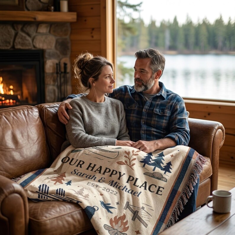 Couple using a personalized Our Happy Place woven blanket in a lakeside cabin